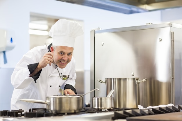 Smiling head chef tasting food from ladle