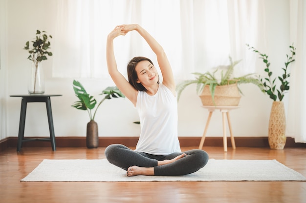 Smiling healthy Asian woman doing yoga shoulder stretching at home