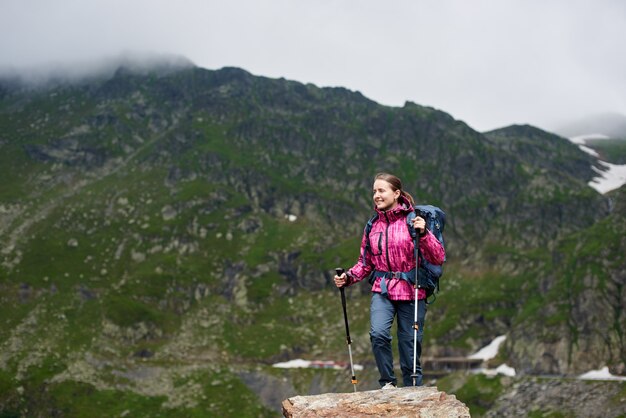 Smiling hiker woman climbing green rocky mountains