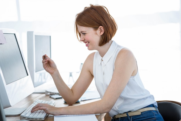 smiling hipster business woman, sitting at her desk, typing her card details 