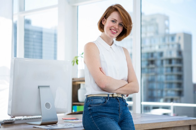 smiling hipster business woman sitting on her  desk with her arms folded