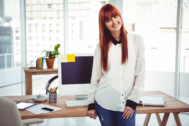 Foto parte anteriore sorridente della donna di affari dei pantaloni a vita bassa del suo scrittorio