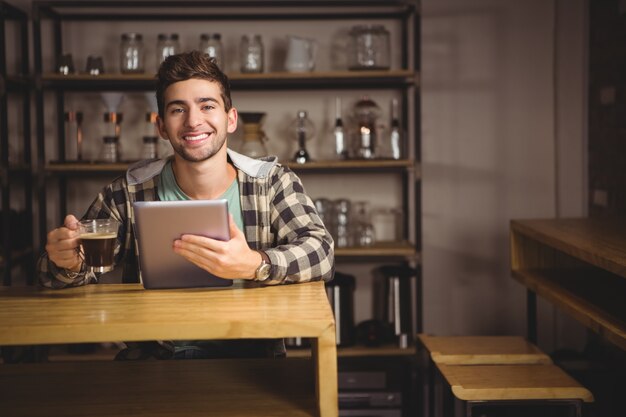 Smiling hipster having coffee and holding tablet computer