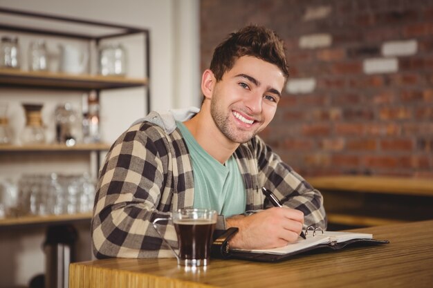 Pantaloni a vita bassa sorridenti che mangiano caffè e che scrivono nel pianificatore