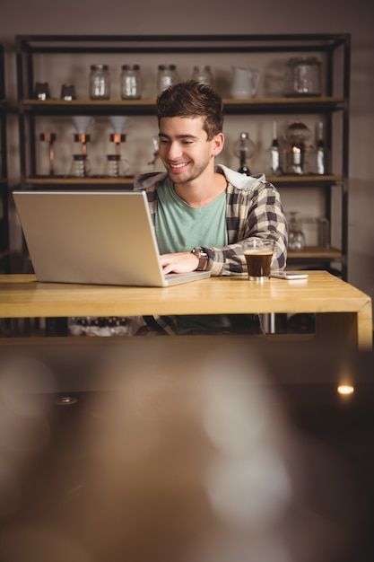 Hipster sorridente che si siede e che utilizza computer portatile