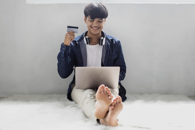 Smiling hipster style consumer looking at laptop while showing his credit card sitting