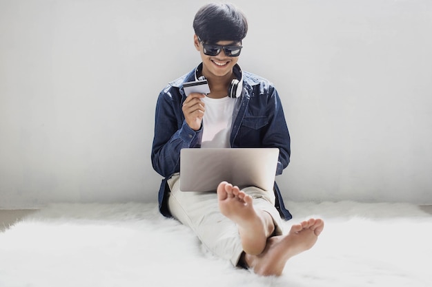 Smiling hipster style consumer shopping via online shop sitting on white fluffy carpet