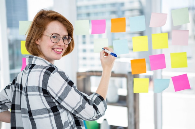 smiling hipster woman in her office, sticking notes to a wall