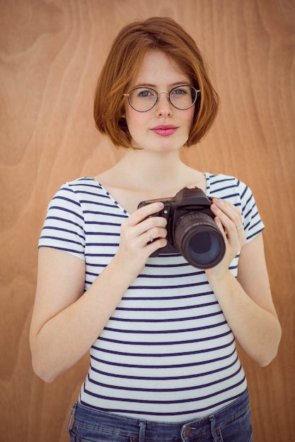 smiling hipster woman holding a digital camera against a  wood