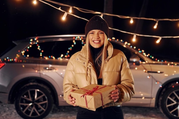 Sorridere e tenere il regalo donna in piedi nella foresta e festeggiare il nuovo anno