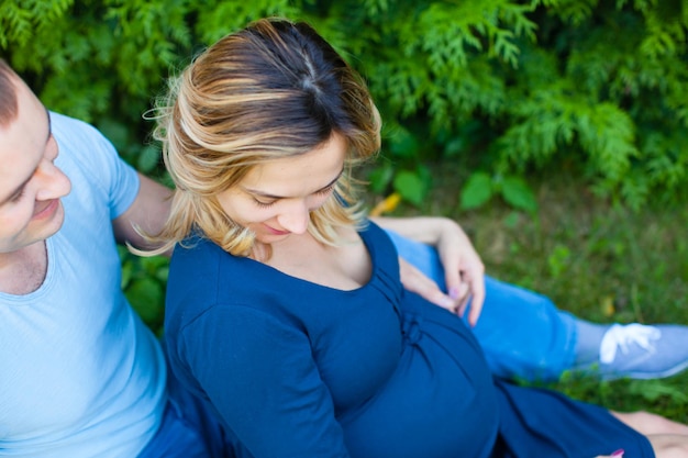 Smiling husband with pregnant wife is resting on the nature