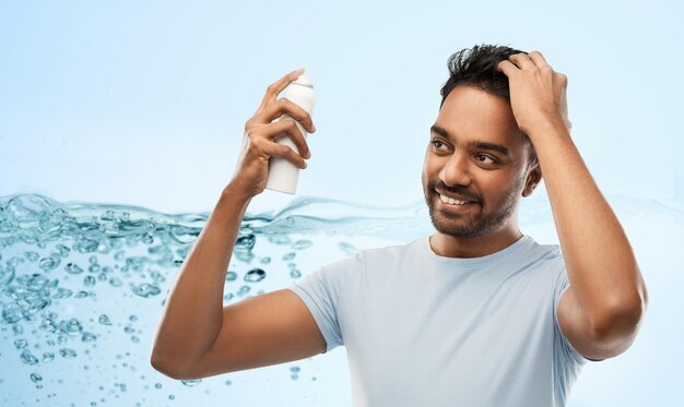 Photo smiling indian man applying hair spray over gray