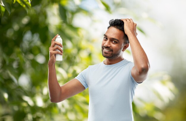 Photo smiling indian man applying hair spray over gray