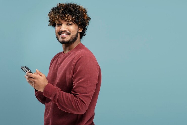 Photo smiling indian man holding smartphone using mobile app shopping online isolated on blue background,
