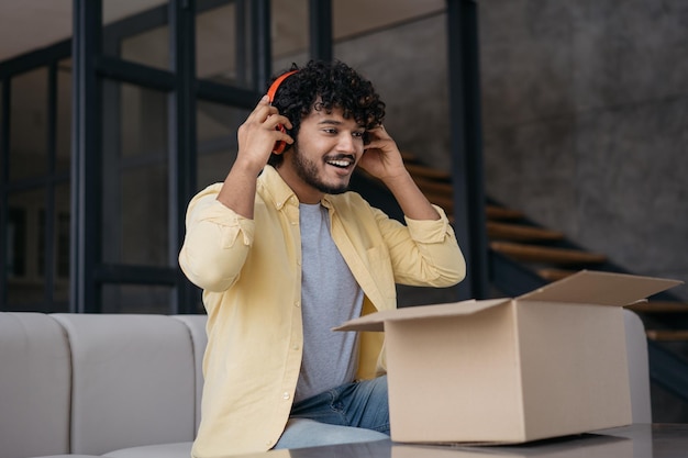 Smiling Indian man unpacking box with present holding headphones listening music Delivery concept