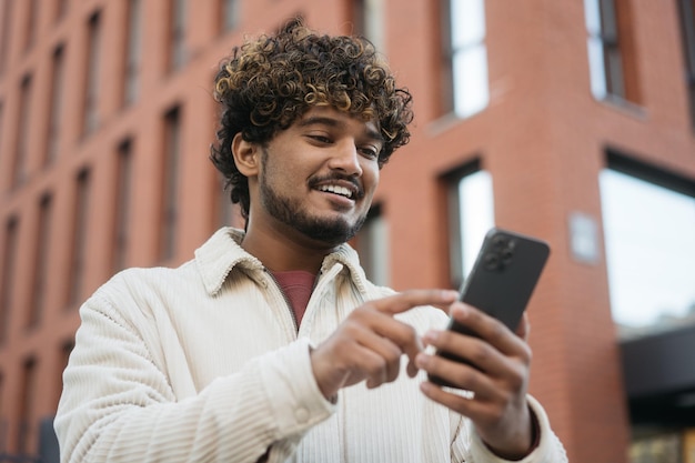 Foto uomo indiano sorridente che utilizza l'app mobile per lo shopping online per strada. ragazzo hipster che tiene il cellulare