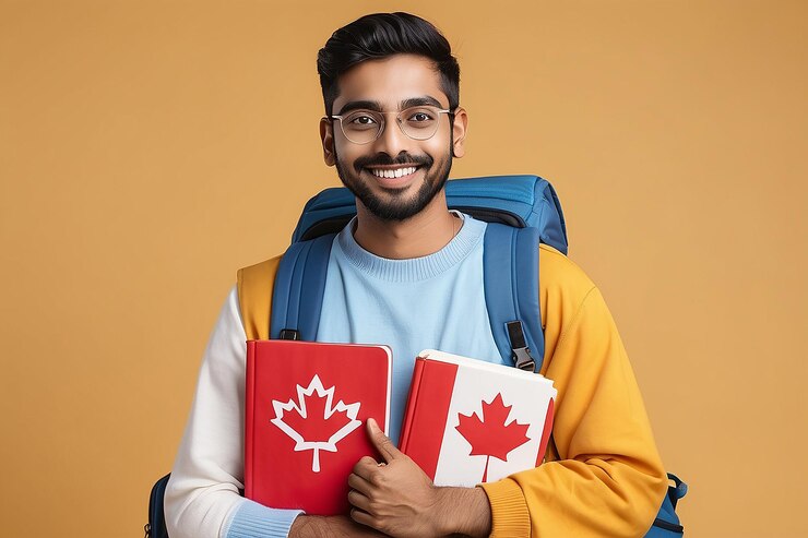 Smiling Indian Man With Canadian Flag And Workbooks In Hands Posing On Yellow Studio Background Happy Millennial Student Guy With Backpack Enjoying Foreign Language Courses And Study Abroad