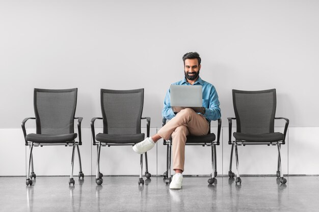 Foto uomo indiano sorridente con laptop nella sala d'attesa dell'intervista