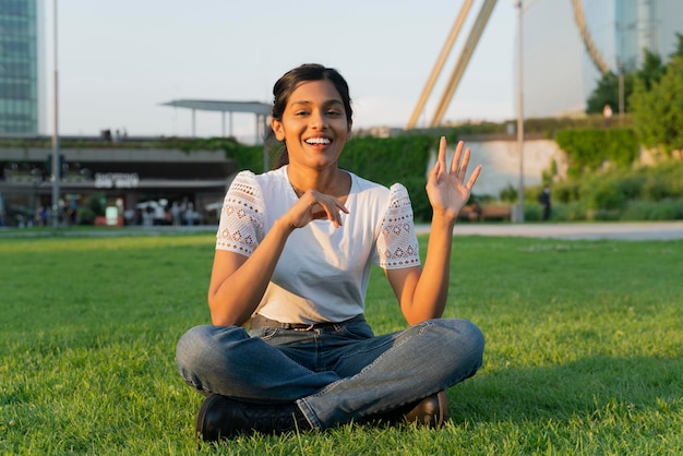 Smiling Indian student using wireless technology having online lesson sitting on grass