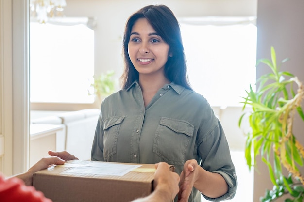 Smiling indian woman customer buyer receiving courier delivery box at home