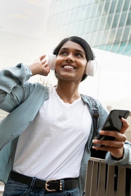 Smiling Indian woman using smartphone wearing  modern headphones listening music walking outdoors