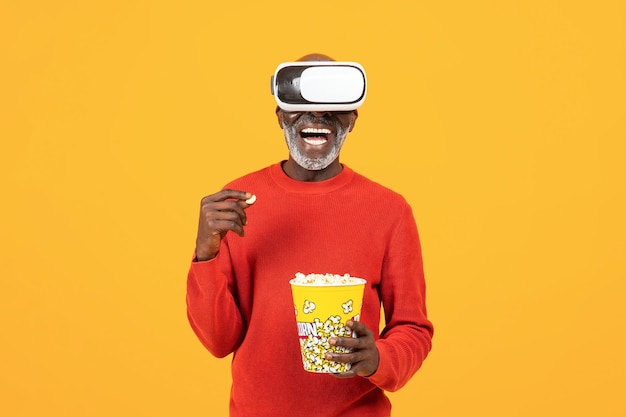 Smiling inspired senior african american man in vr d glasses eat popcorn watch film