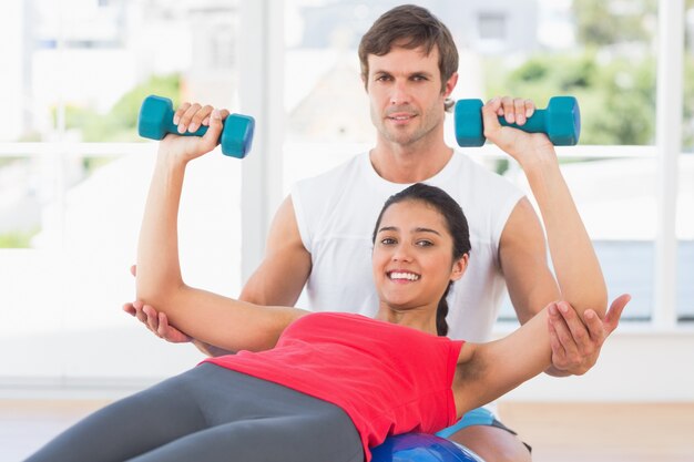 Smiling instructor with woman lifting dumbbell weights