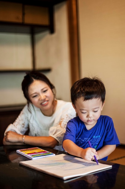 Smiling Japanese woman and little boy drawing on white paper