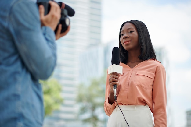 Smiling journalist and cameraman filming news report for tv show