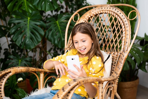 Smiling kid girl communicates online sitting on rocking chair at home