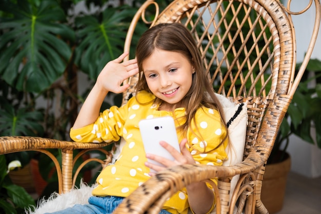 Smiling kid girl communicates online sitting on rocking chair at home