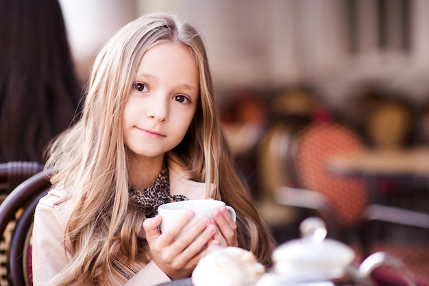 Smiling kid girl drinking tea in cafe outdoor