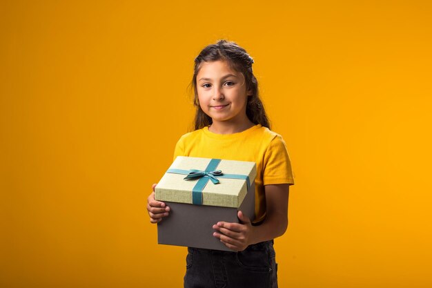 Foto ragazza sorridente che tiene una scatola regalo su uno sfondo giallo concetto di compleanno e celebrazione