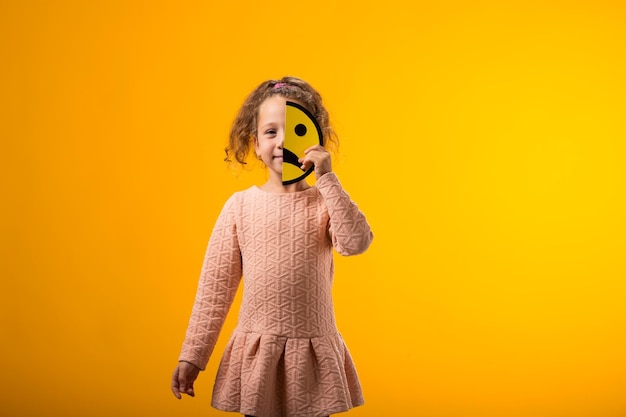 Smiling kid girl holding sad half face emoticon Mental health psychology and childrens emotions concept