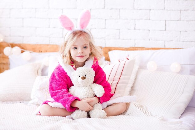 Smiling kid girl holding teddy bear sitting in bed