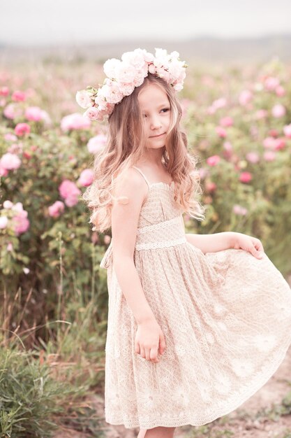 Smiling kid girl posing in rose garden wearing stylish dress