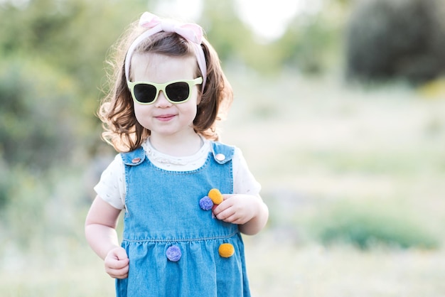 Smiling kid girl wearing sun glasses and denim dress outdoors