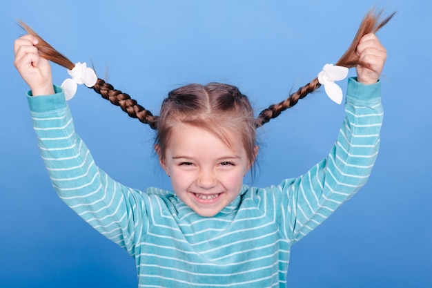 Smiling kid girl with two braids having fun over blue background