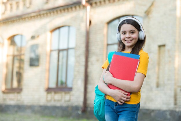 笑顔の子供はフォルダを保持しますヘッドセットで子供の頃の幸せの女の子は音楽を聴きます電子ブックから知識を得る現代の学校教育から学校に戻る幸せなティーンはワークブックを運ぶ