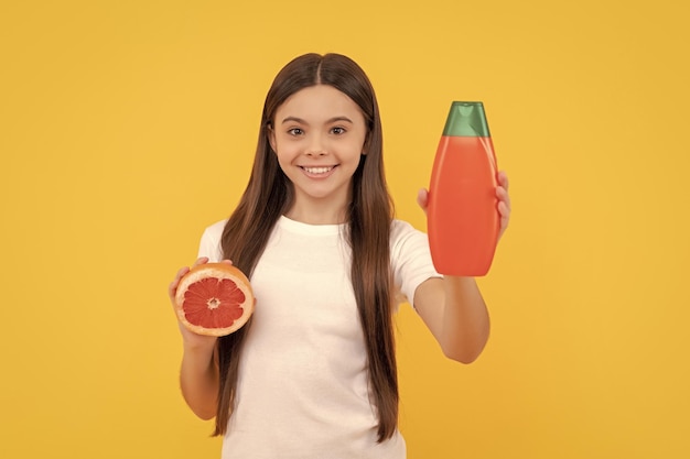 Smiling kid hold hair conditioner bottle and grapefruit on yellow background citrus