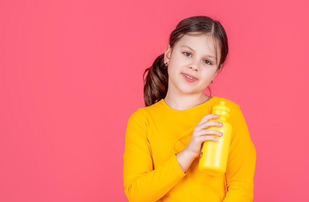 笑顔の子供がピンクの背景に水のボトルを保持します。