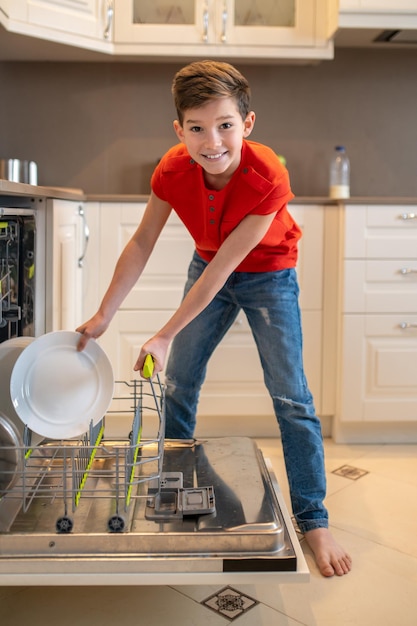 Smiling kid preparing dishes for cleaning in a dishwasher