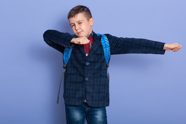 Smiling kid on a suit with a schoolbag imitating superheroes