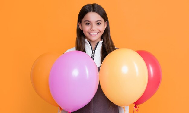 Smiling kid with party colorful balloons on yellow background