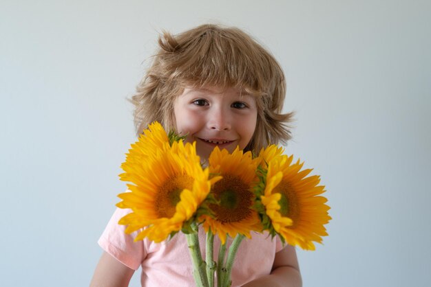 Bambino sorridente con i girasoli. bambino felice con bouquet di fiori. ragazzo carino adorabile romantico e sorpresa.