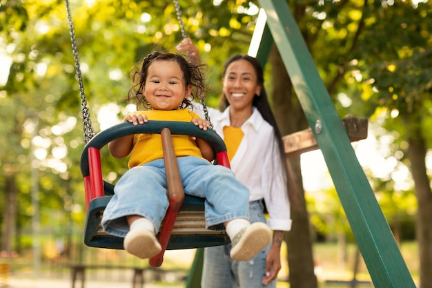 Smiling korean mother swinging baby on swing on playground