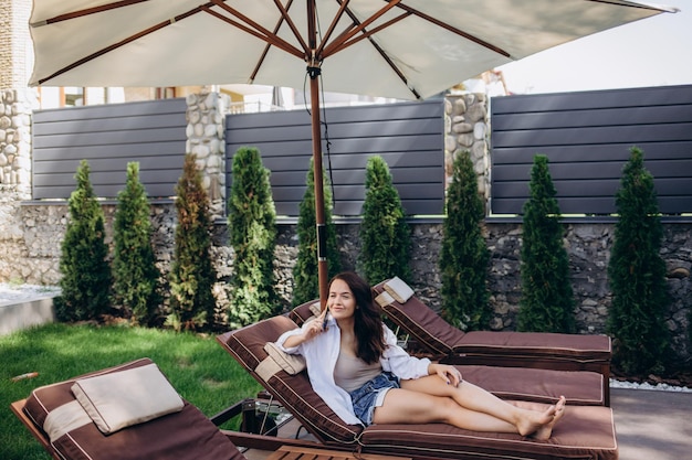 Smiling lady lying on deckchair having call and drinking cocktail on a beach