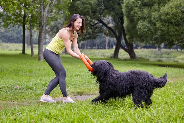 Smiling lady plays with briard in public park.