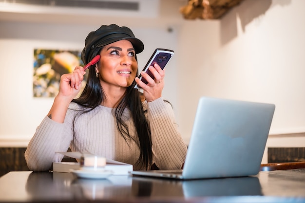 Smiling Latina brunette architect sending work audio note with portable phone from coffee shop