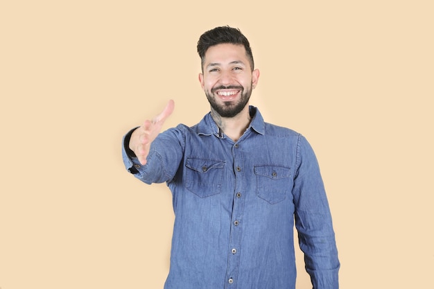 Smiling latino hispanic man makes welcome gesture on yellow background